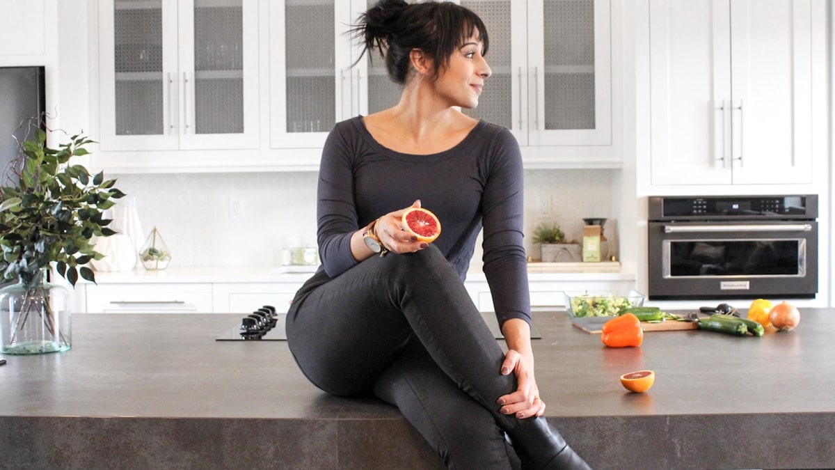 a woman sitting on a kitchen counter holding a piece of fruit